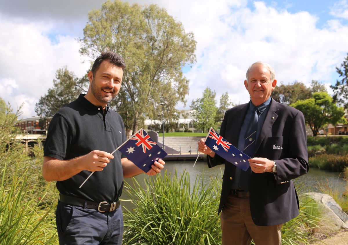 Wagga's Mayor and 2020 Environmental Citizen of the Year holding small Australian flags and standing next to lagoon 