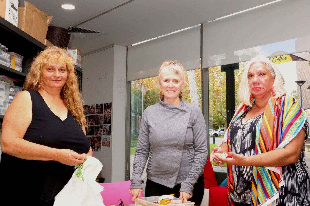 Three women standing around table with colourful cotton thread in hands and on table