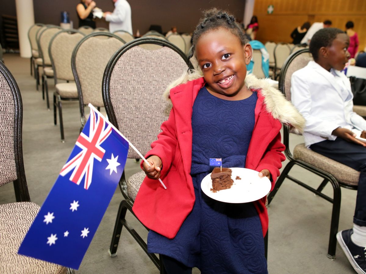 Young girl holding a small Australian flag in one hand and a cake on a plate in the other
