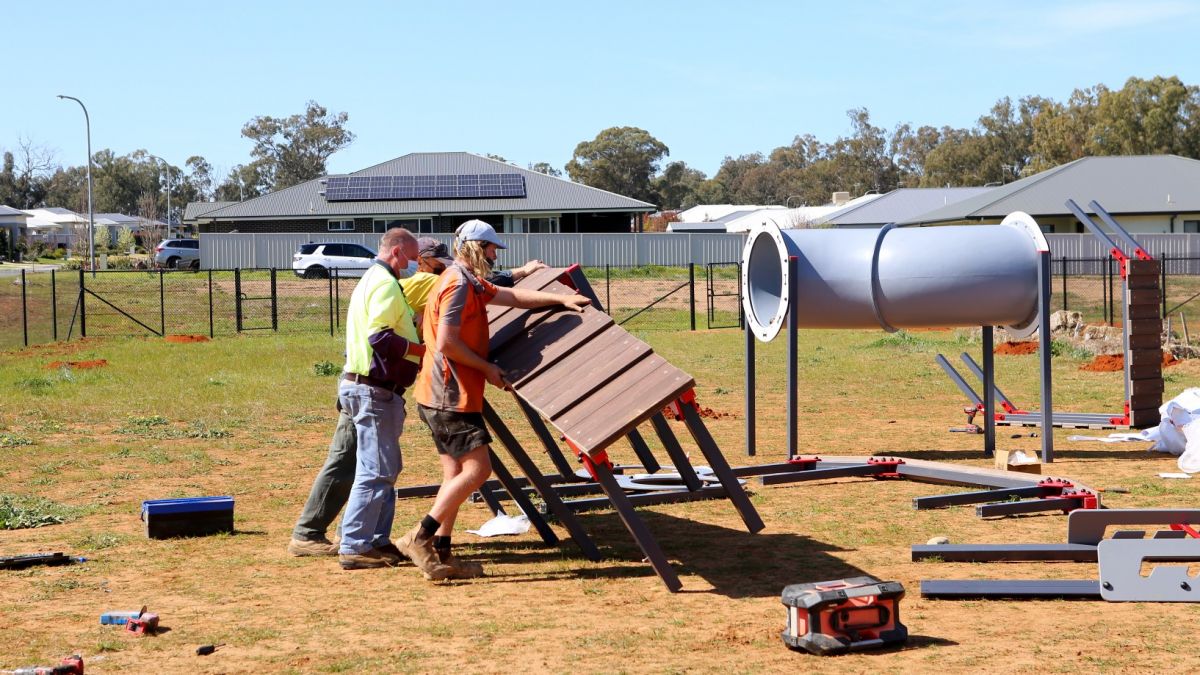 Three men lifting a dog agility ramp upright