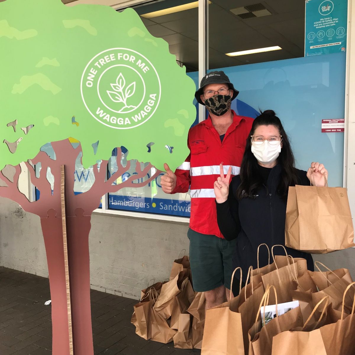 man and woman holding paper bags and standing next to a cardboard cutout tree