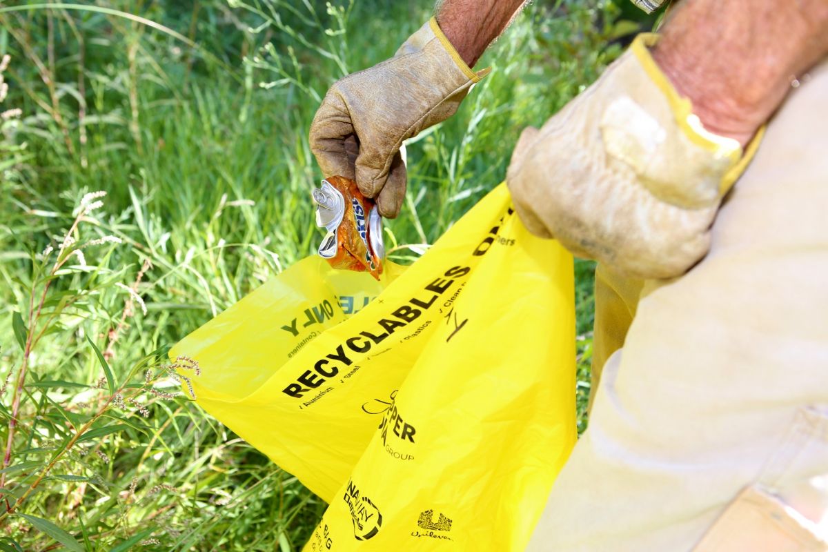Hand holding yellow Clean Up bag, putting in can