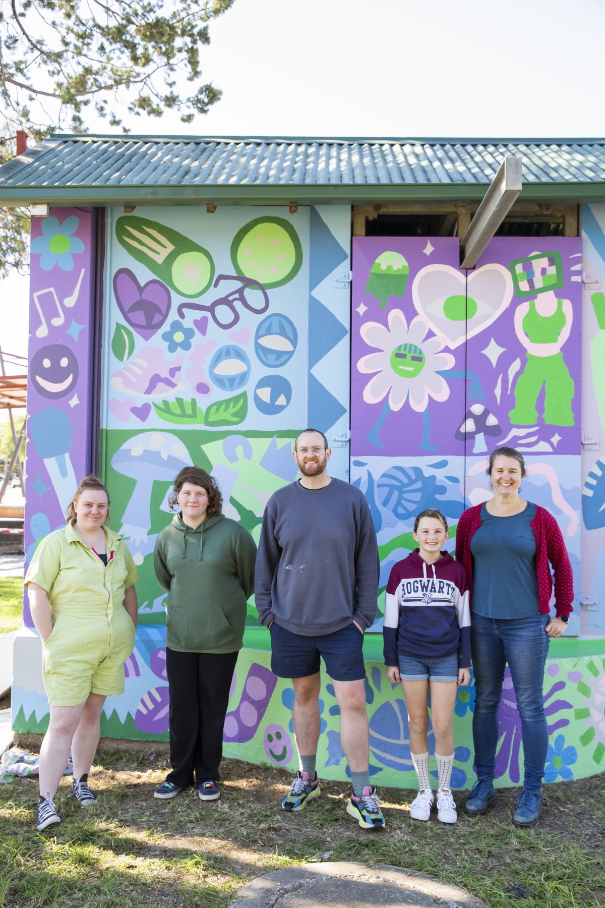 Three young females, older female and man standing next to mural on pump station