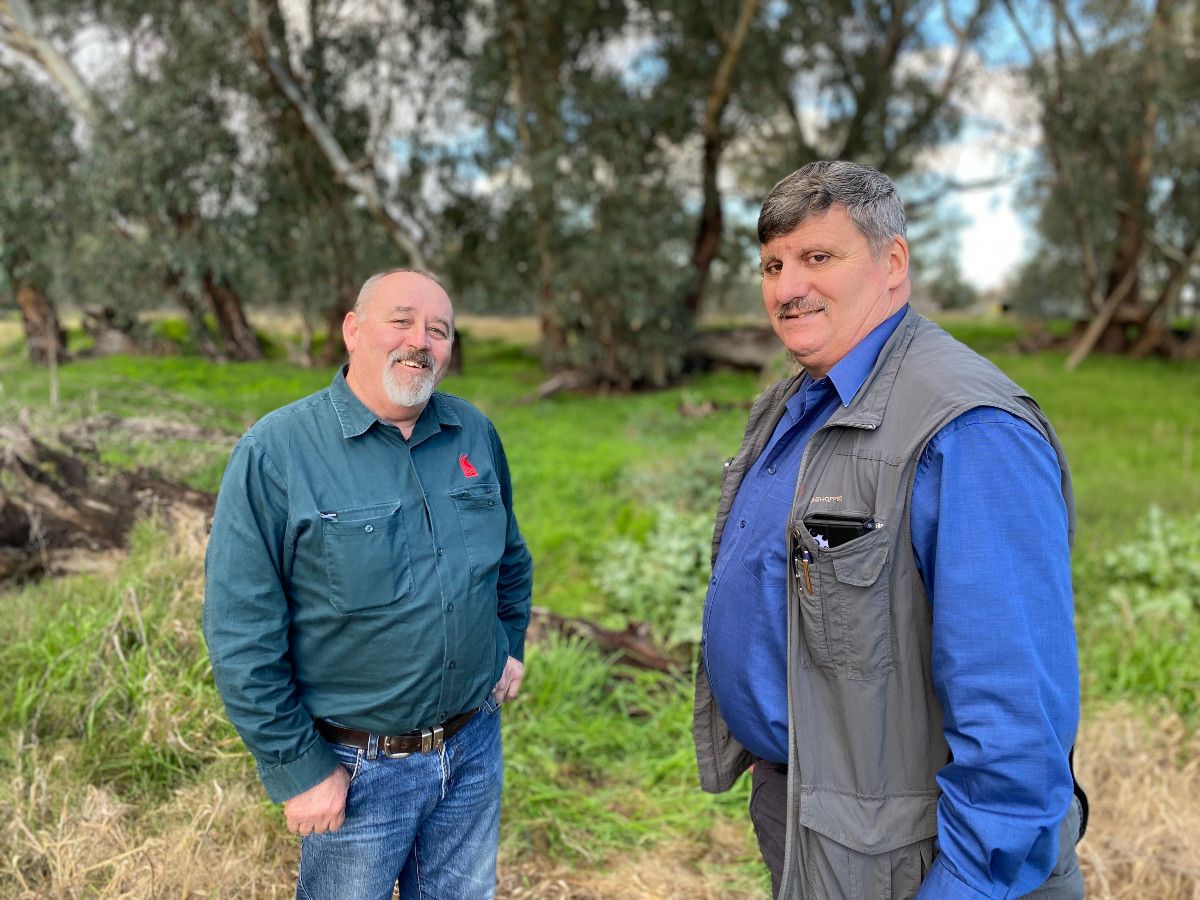 Two men stand in a green rural setting