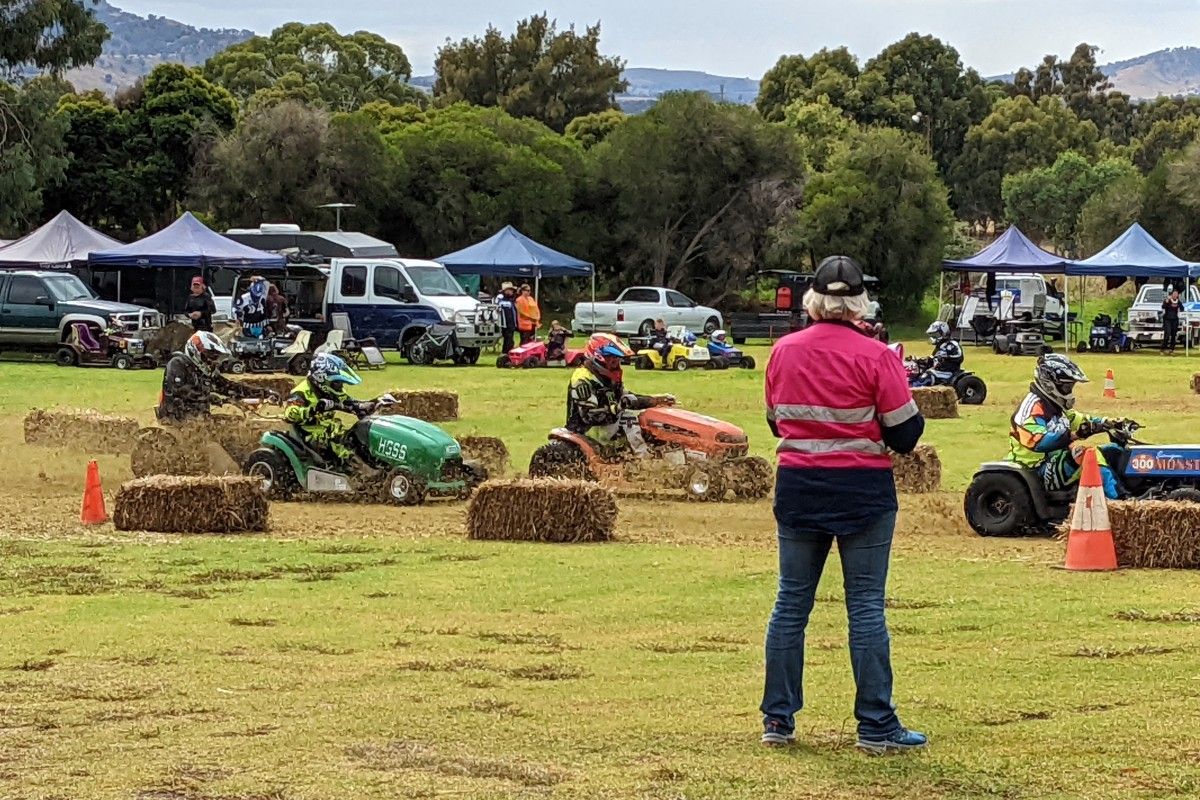 Man standing beside track with ride on lawn mower racing