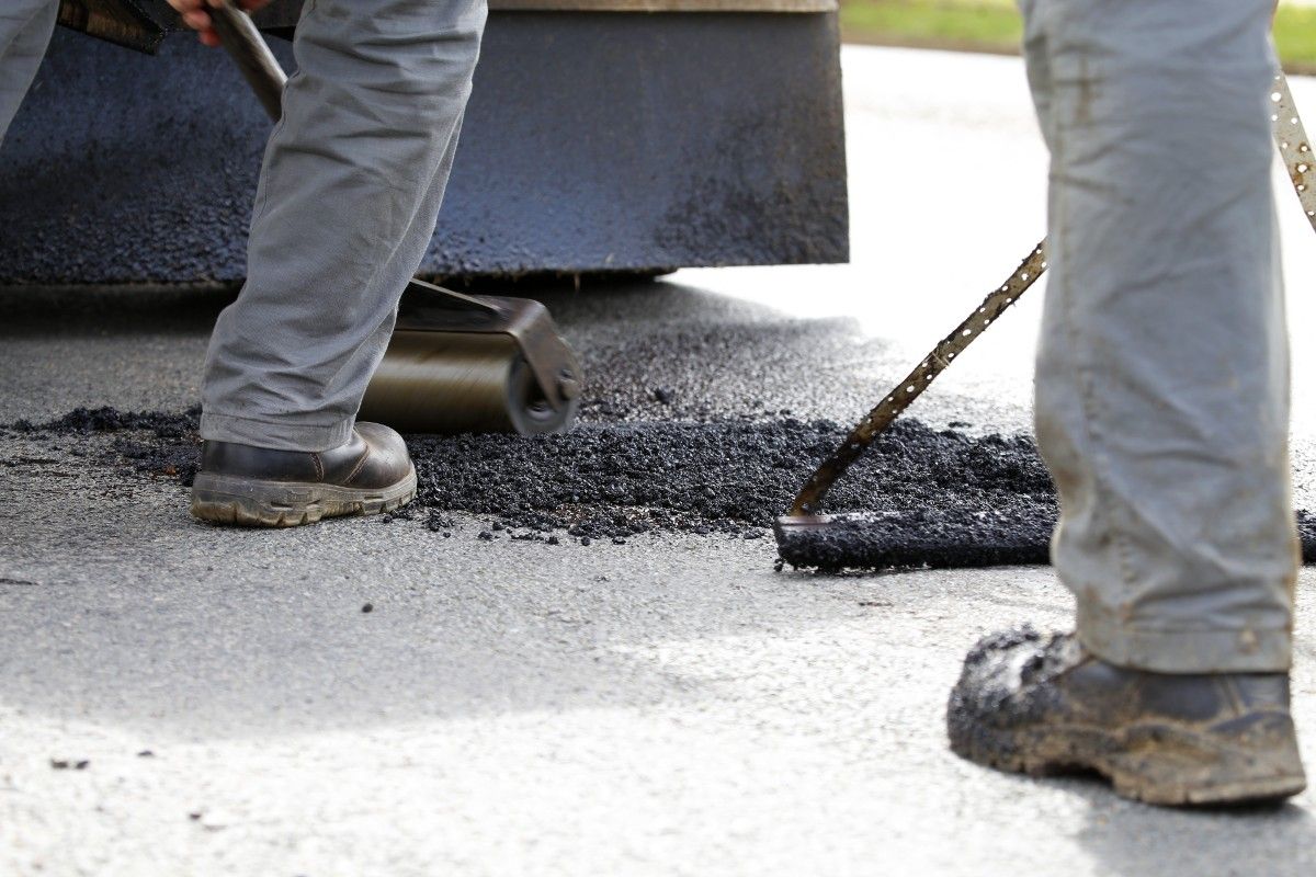 Road crew shovelling bitumen into pothole in suburban area Council News Socials