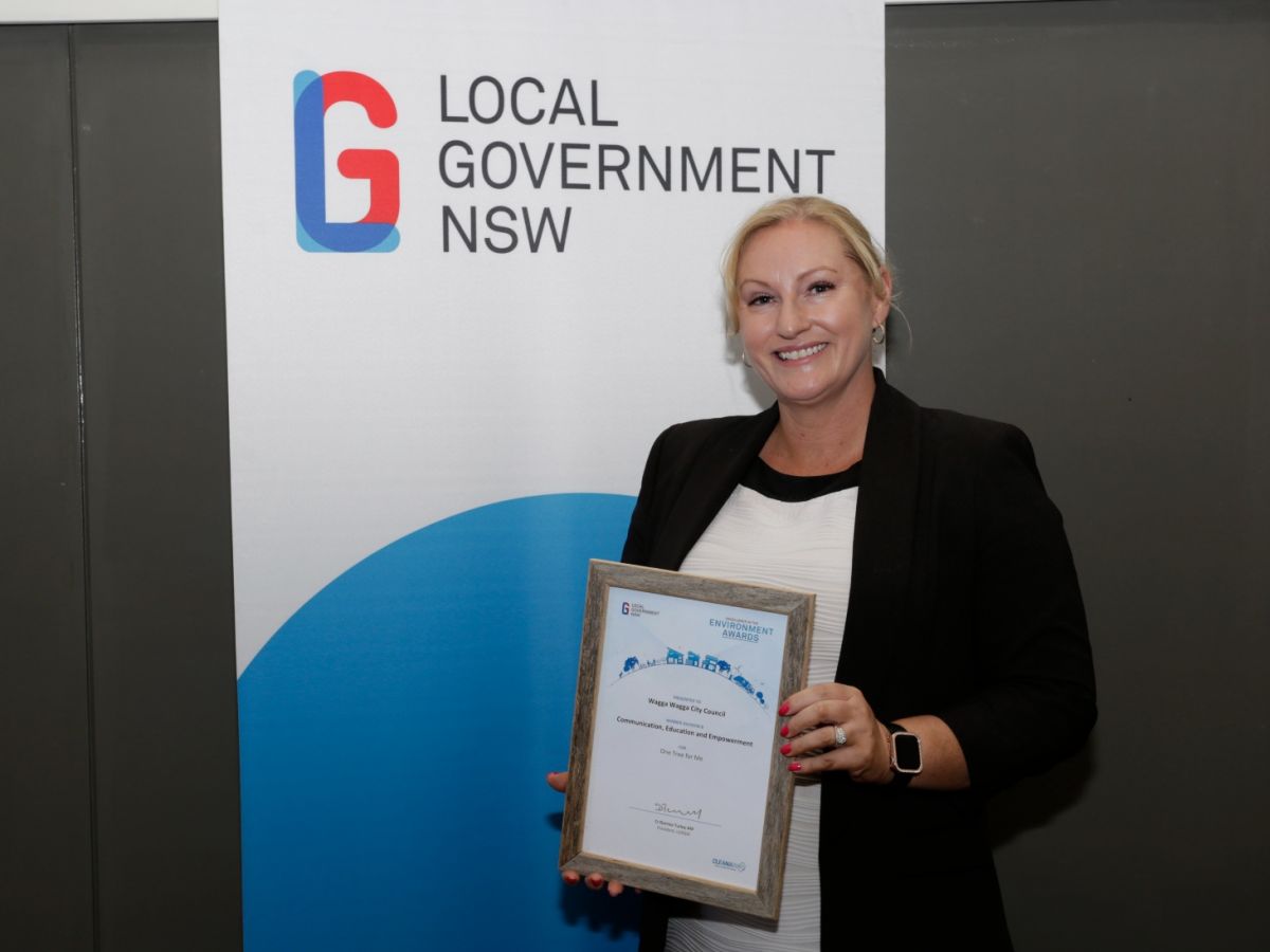 Carly Hood holding award, with Local Government NSW banner in background