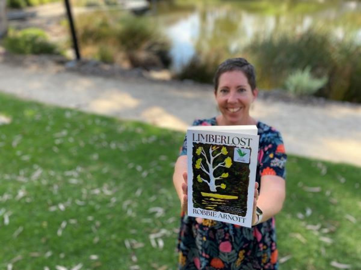 A woman in a park holds out a book