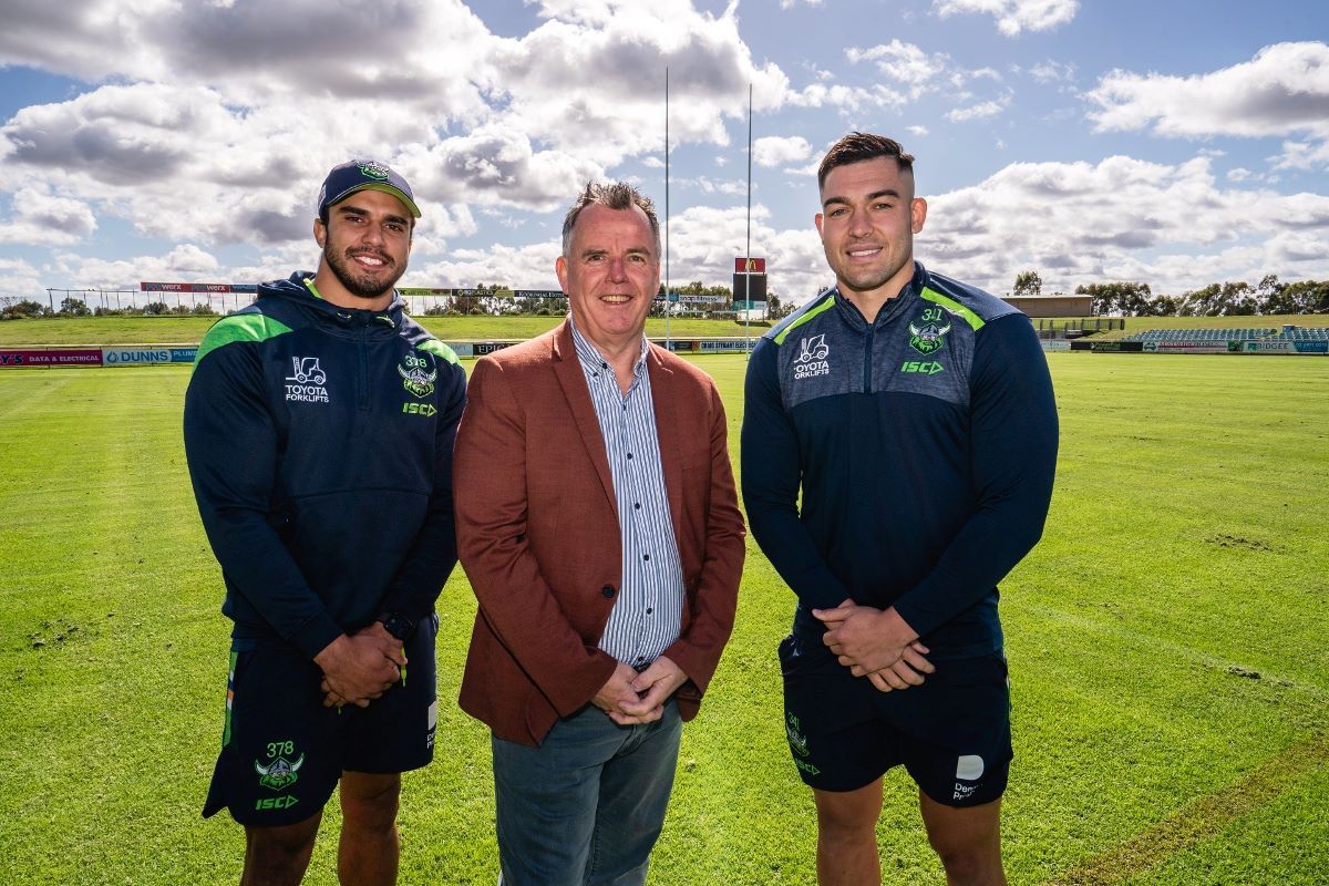 Two Raiders football players with Wagga Mayor on football field