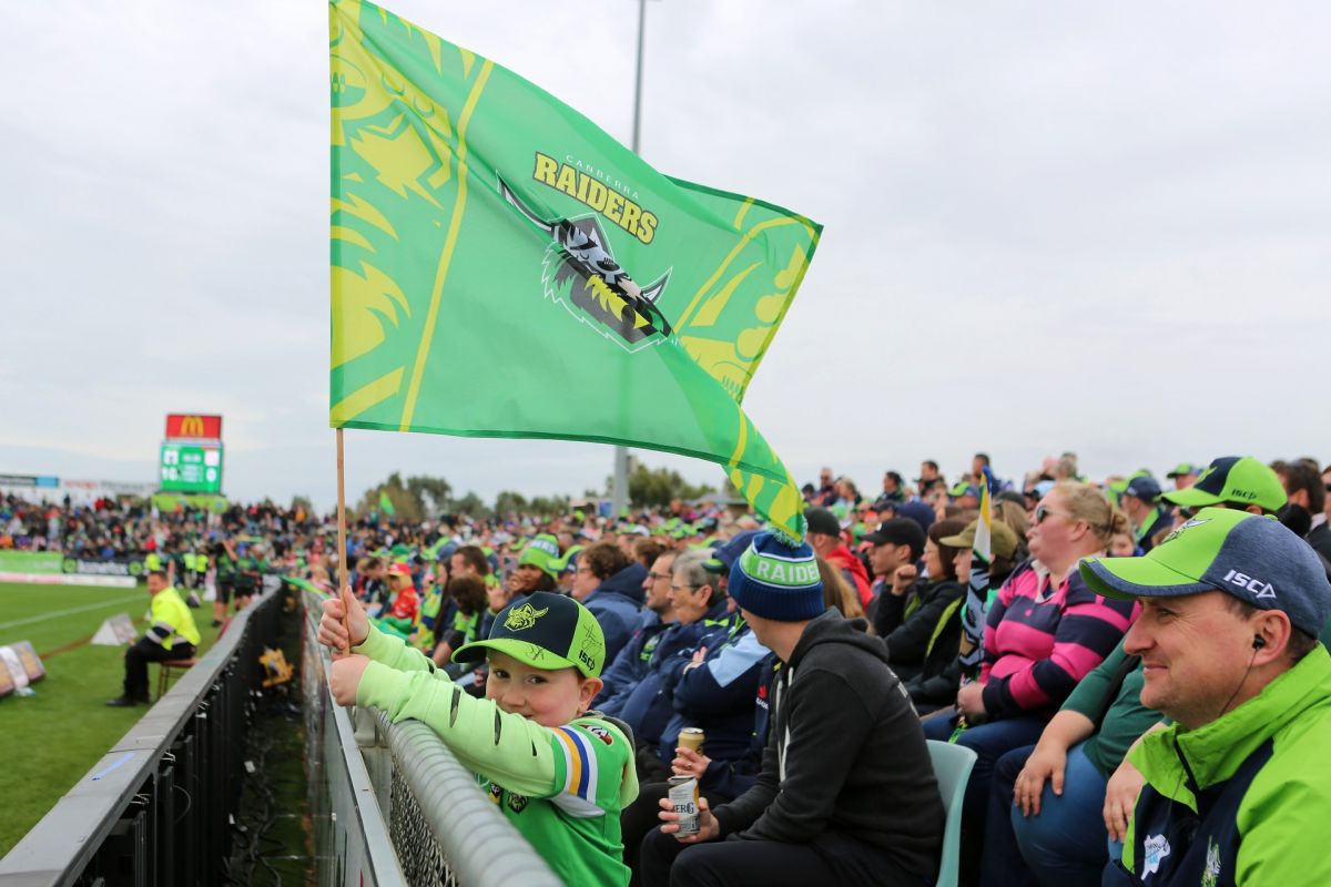 Young boy looking at camera while waving Raiders flag, with crowd beside and behind him