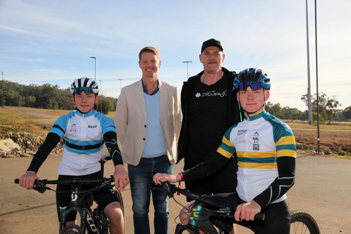 Two young cyclists with bikes and two men, with criterion track in background