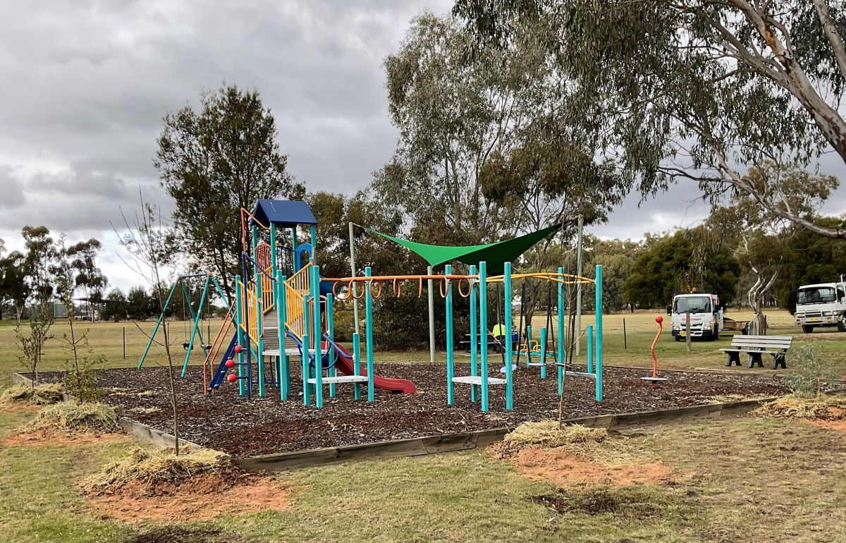 A playground with newly planted trees around the perimeter. 