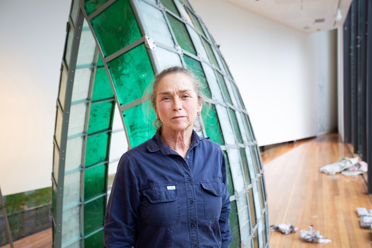 A woman stands in front of a large arc shaped structure made from metal and glass in an art gallery. 