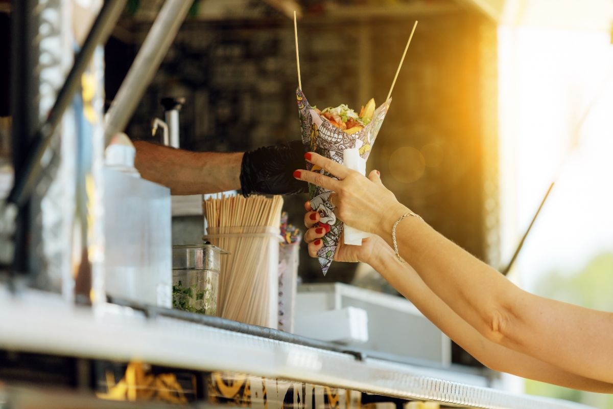 Street food truck's female customer's hands reaching for salad wrap being handed to her through the serving area of the truck.