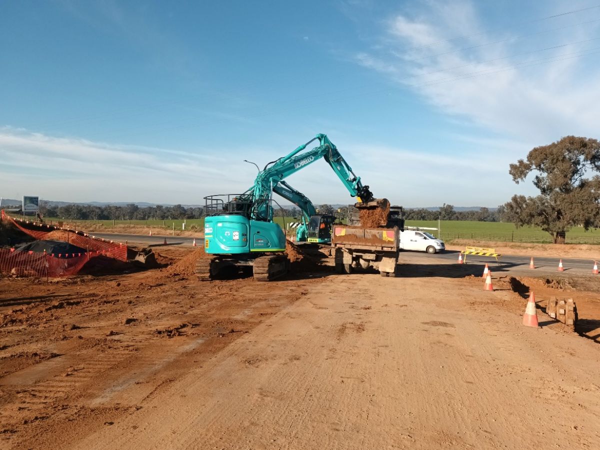 Excavator putting dirt into back of truck at roadworks site.