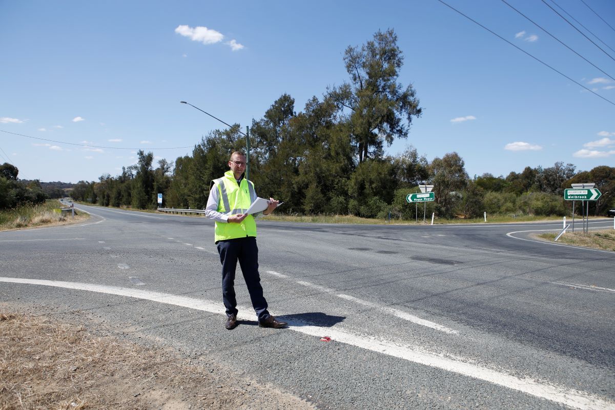A man stands next to an intersection on a country road. 