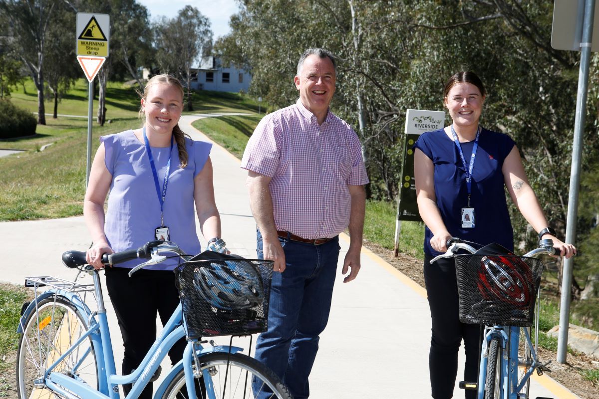 Two young women and a man with bicycles in an outdoor area. 