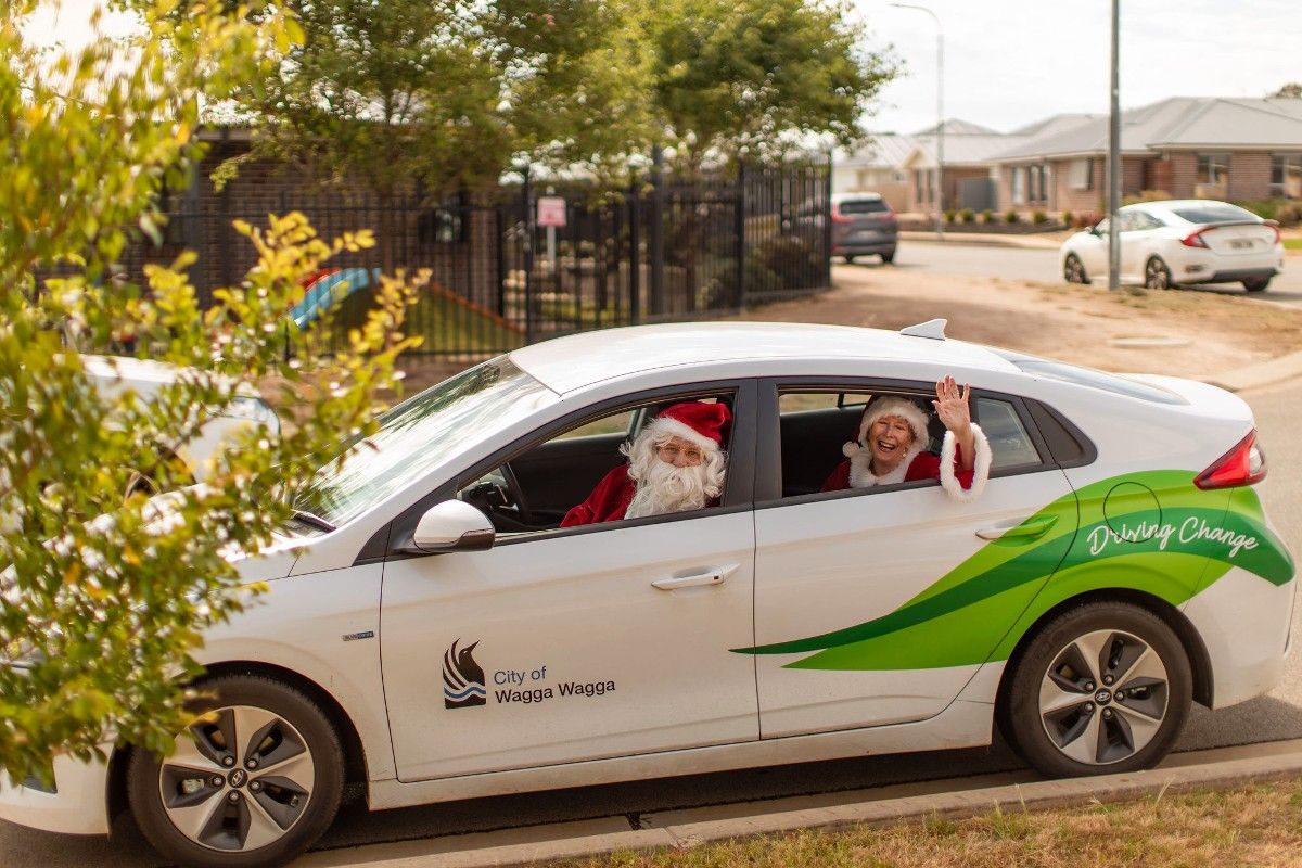 Man and woman dressed as Santa and Mrs Claus looking out the windows of an electric vehicle