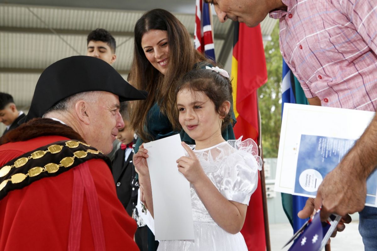 Man in mayoral robes of red hands certificate to young girl in white dress