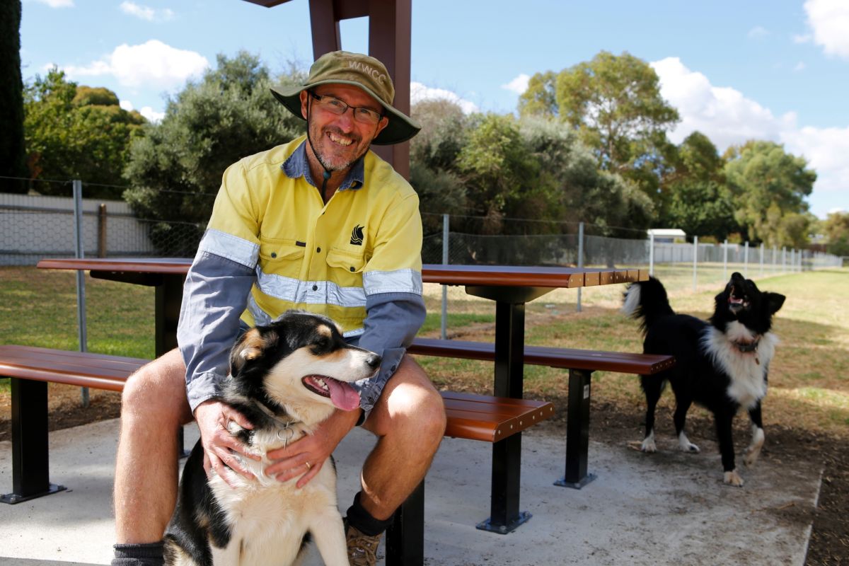 Parks and Recreation Assets Officer Rob Owers, and dogs Leo and Teddy sit on the new picnic setting at the dog park.