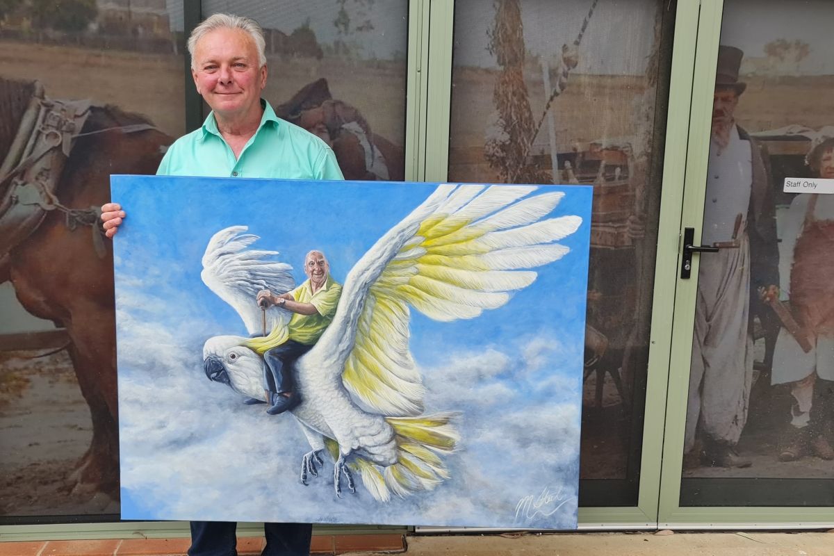 Museum of the Riverina Manager Luke Grealy holds up Marty Steel’s winning 2023 caricature showing Maude the cockatoo, the Bald Archy’s chief judge, holding aloft the late Peter Batey OAM, the founder of the Bald Archy.