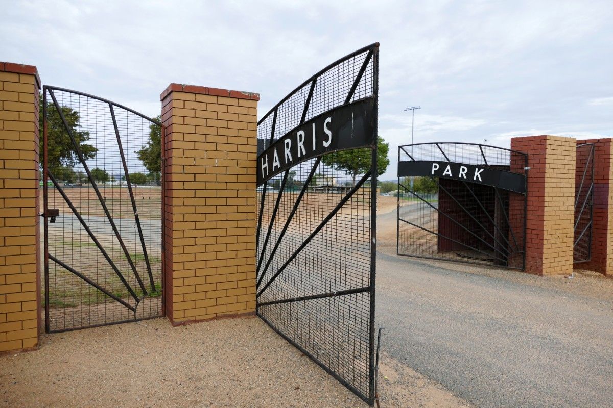 Black metal gates with Harris Park sign in foreground and sportsground in the background.