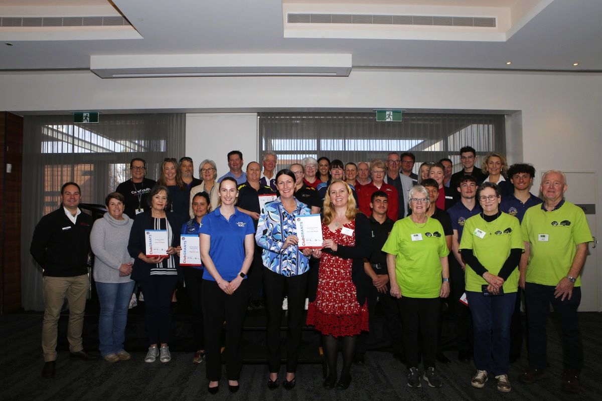A group of males and females standing inn four rows, posing for photo with a number of people holding Clubgrants certificates
