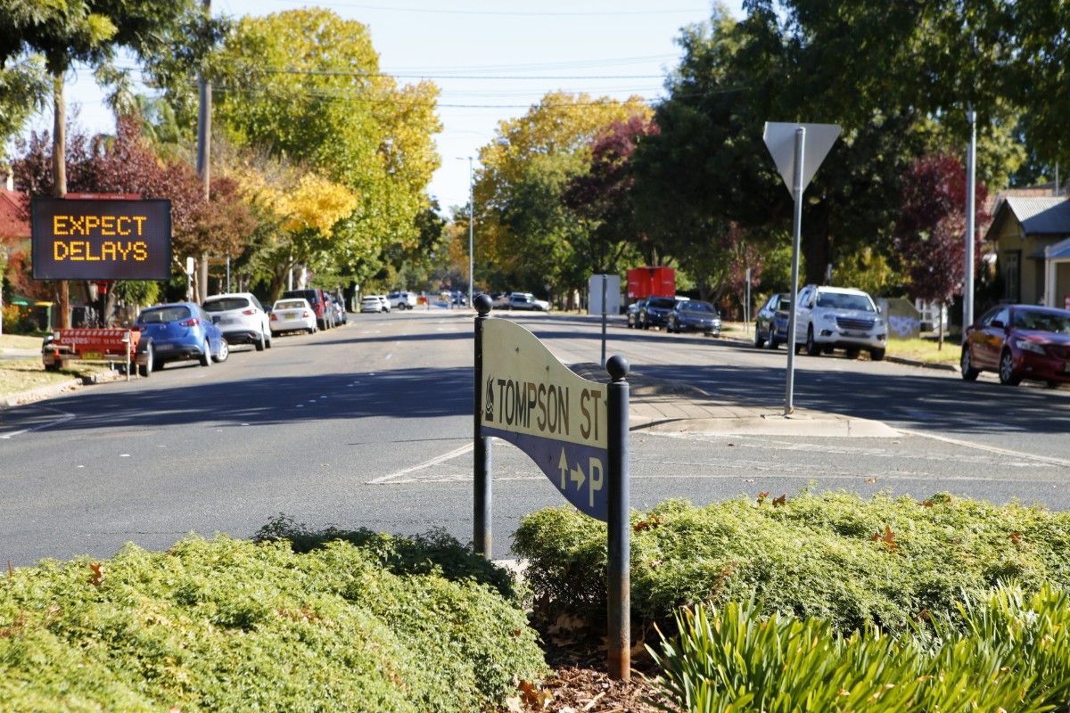 Street sign saying Tompson Street in foreground with road in background, electronic messaging board saying expect delays beside road.