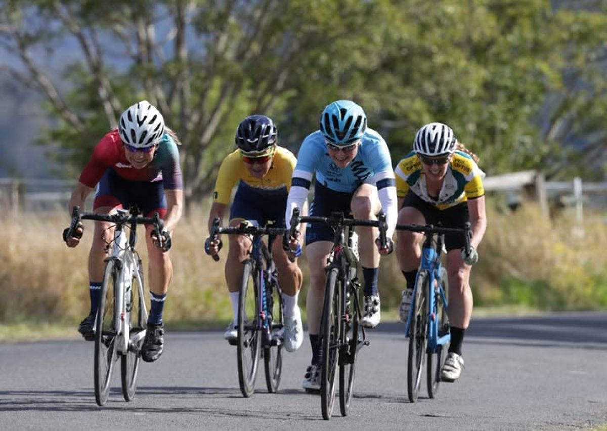 Four road cyclists in colourful shirts and helmets race along a road.