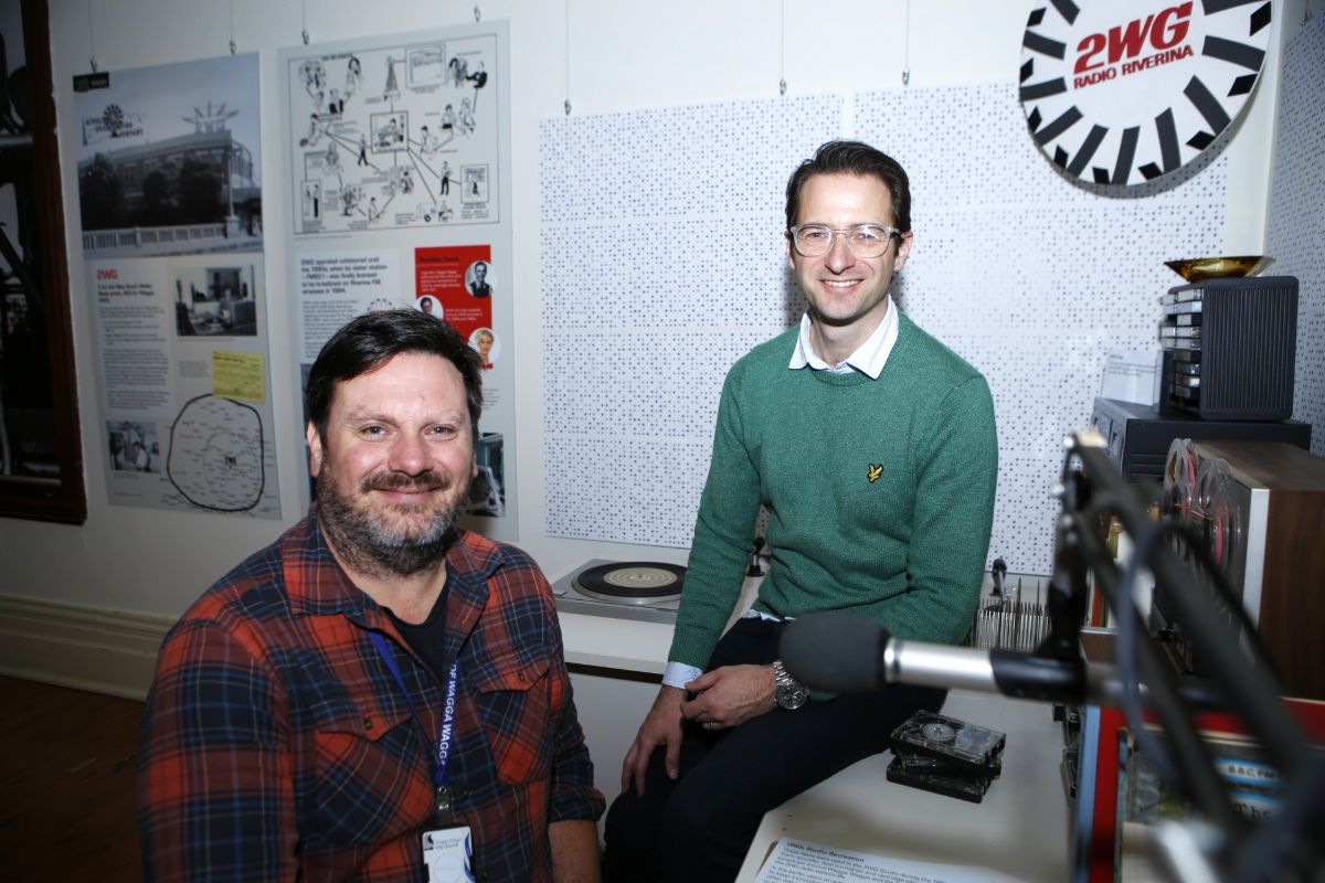 Two men, one with a beard, sitting at a desk featuring old equipment from a radio study as part of a museum exhibition about the Wagga media landscape over 150 years.