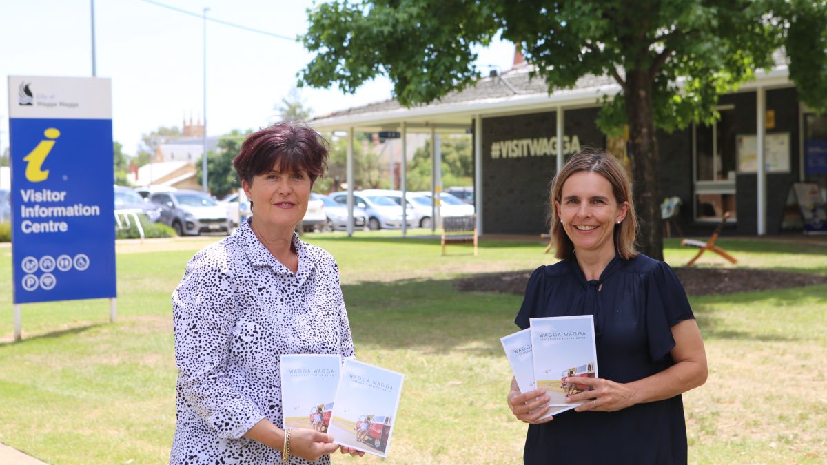 two women holding brochures, standing in front of sign and building