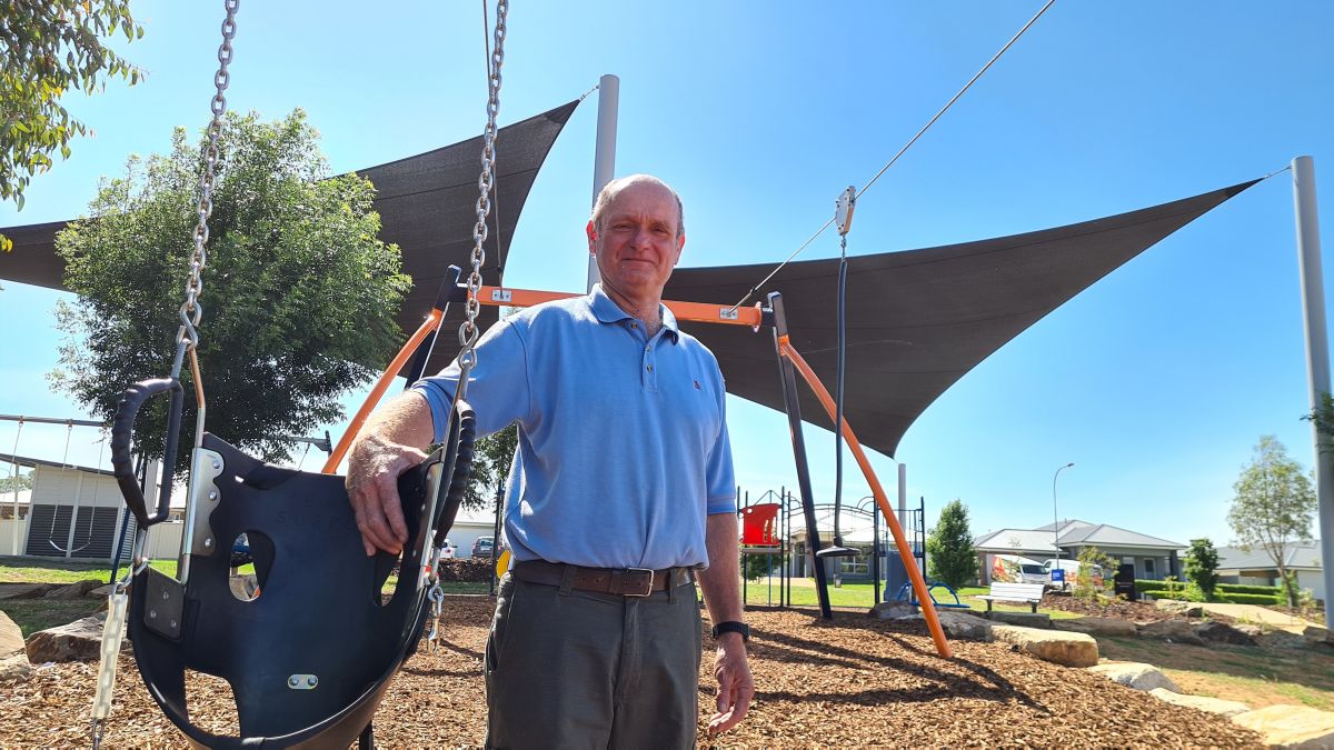 Man standing holding flying fox seat with playground and shade sails in background