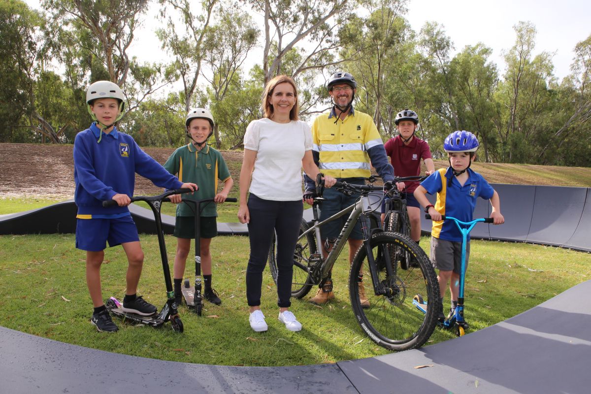 Woman and man with four boys wearing helmets and on scooters and bikes 