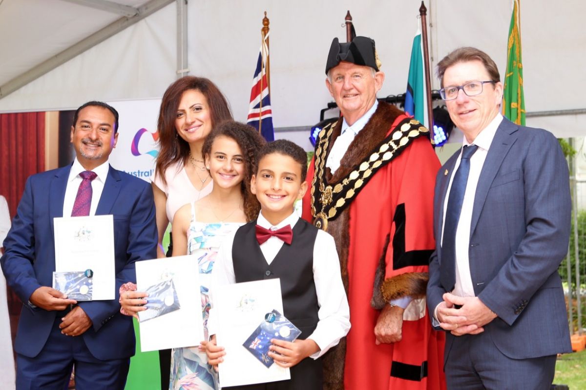 Family holding certificates, standing next man dressed in mayoral robes and man in suit, with flags in background