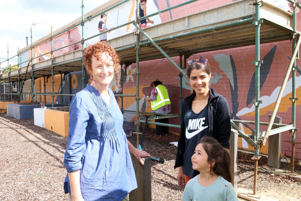 Two women and young girl standing in front of scaffolding and mural being painted on brick wall