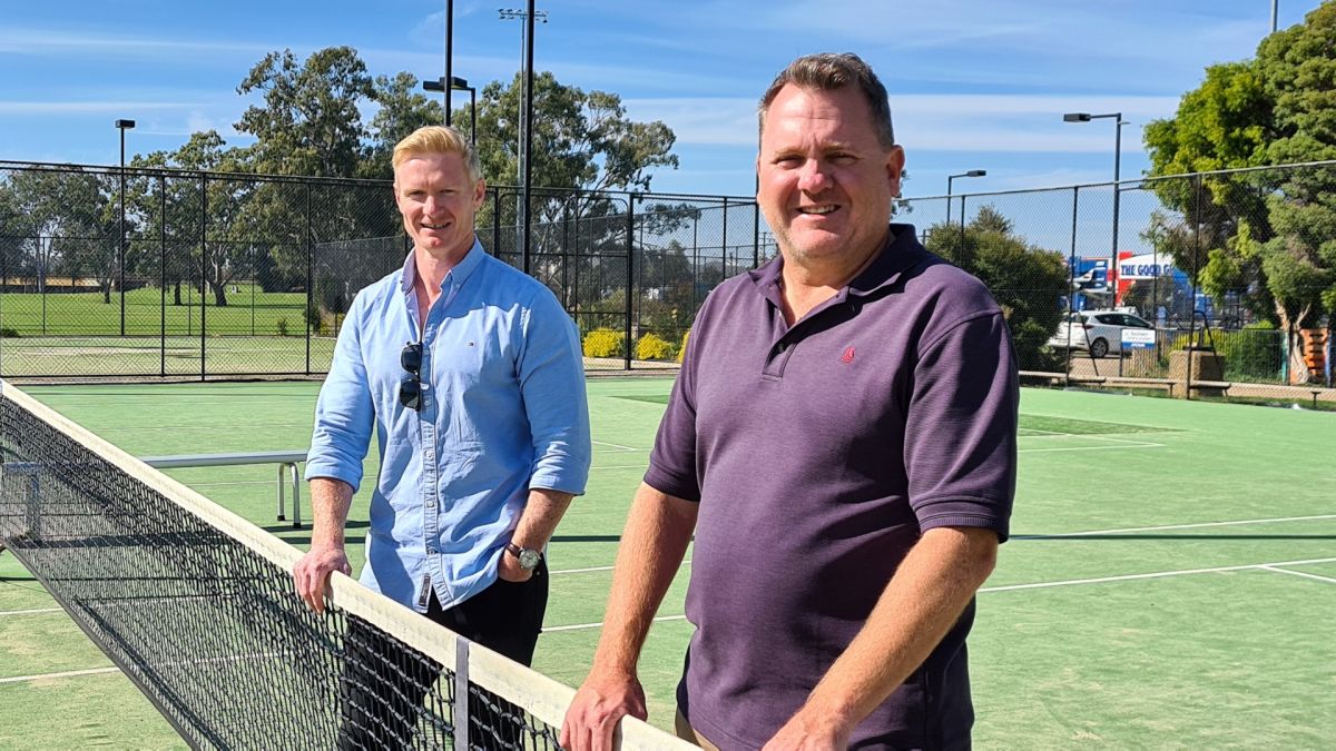 Two men standing with hands resting on net on tennis court