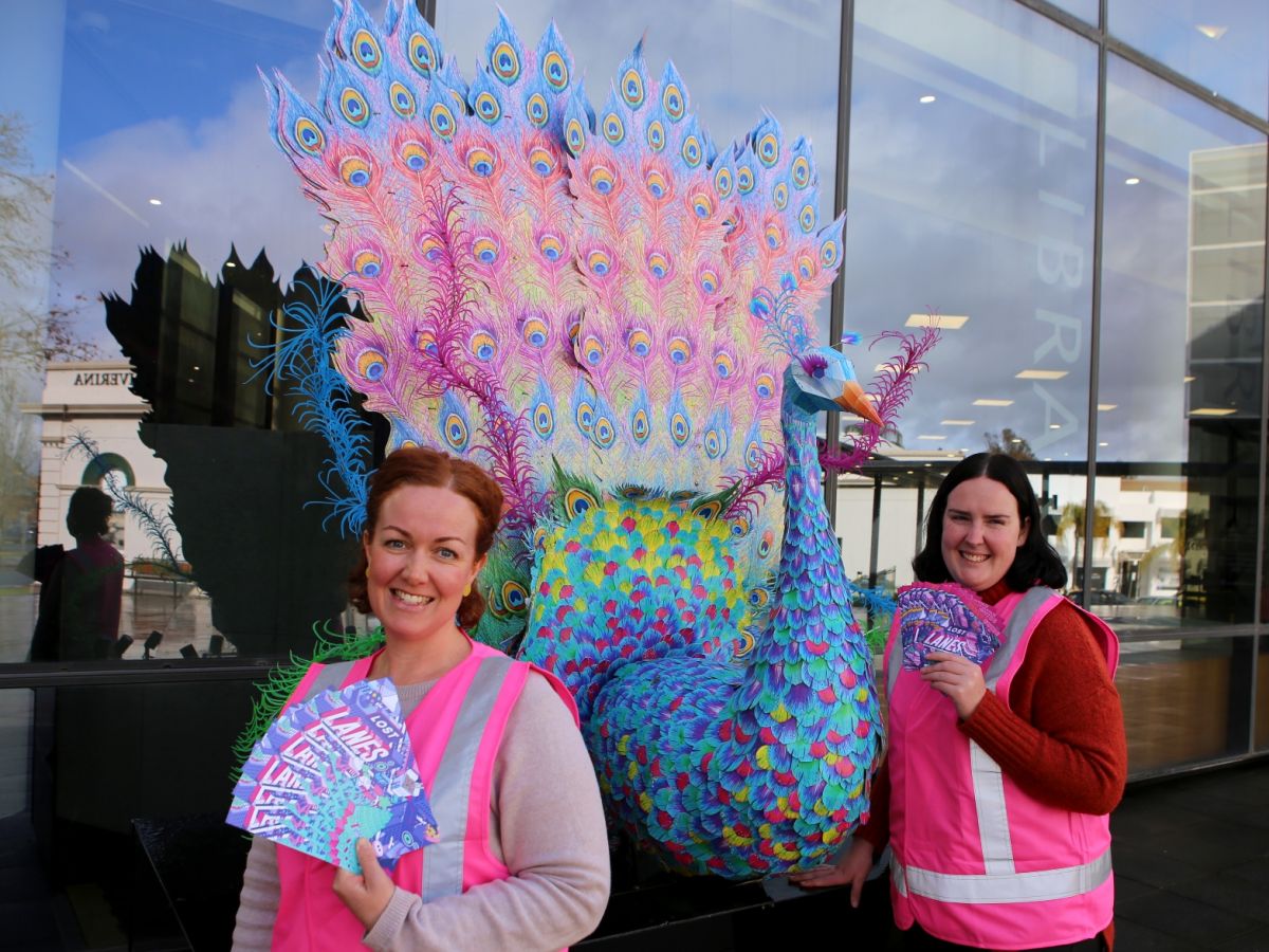 Two women in pink jackets standing in front of peacock sculpture