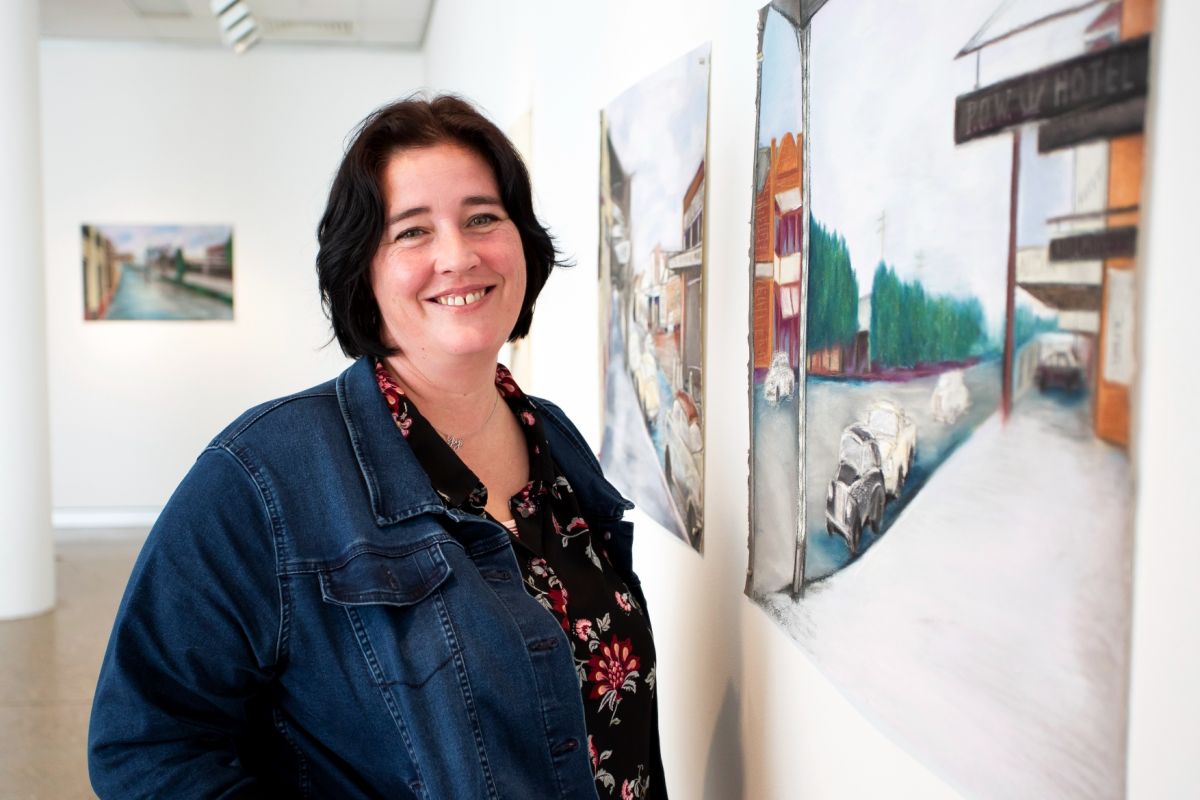 Woman standing next to pastel drawings on chalk boards hanging on art gallery wall