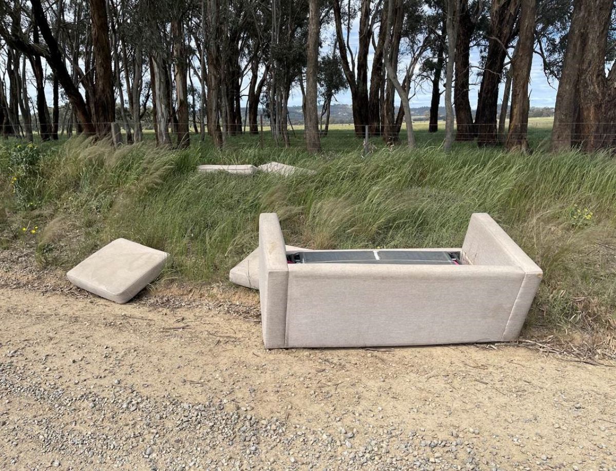 Dumped couch laying on the side of a quiet rural road