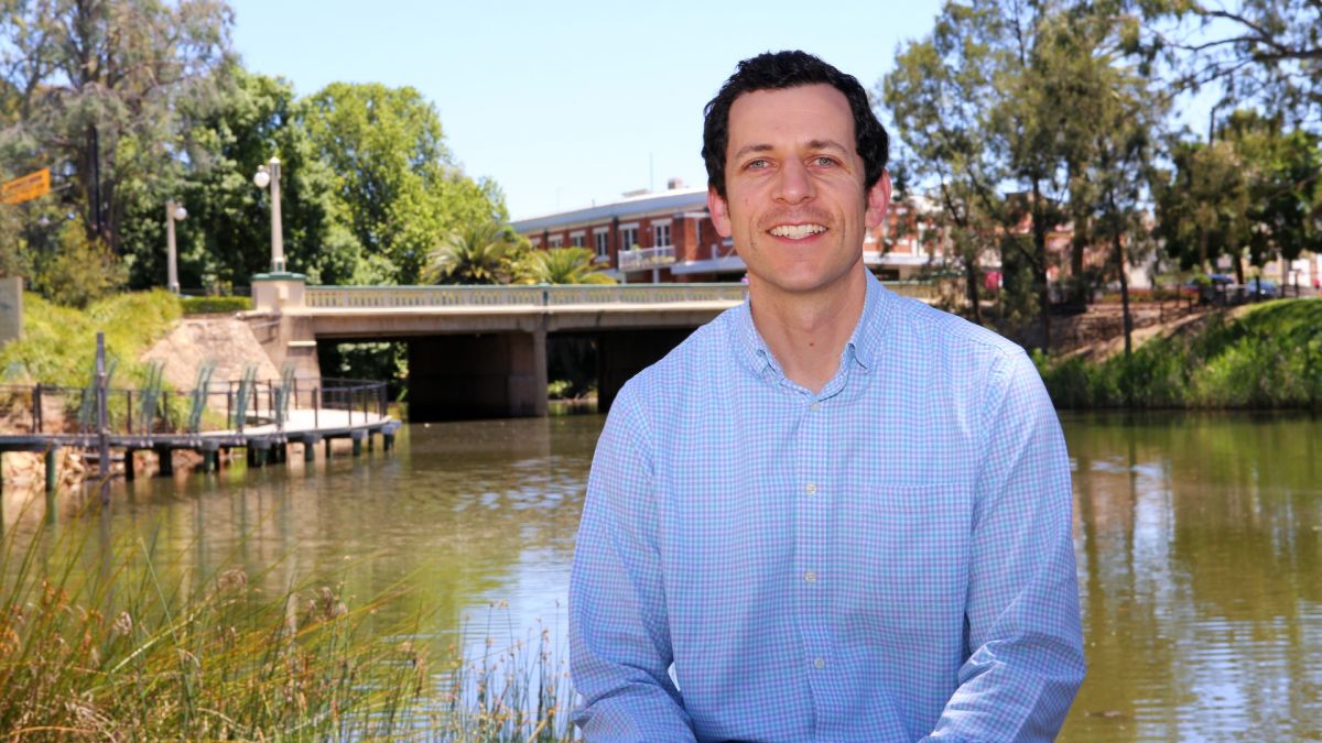 man sitting by lagoon with bridge in background