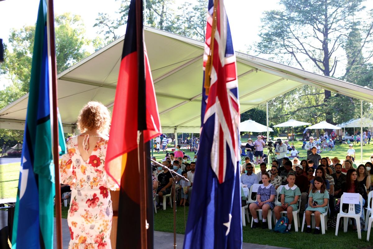 Three flag and back of MC on stage with crowd in background