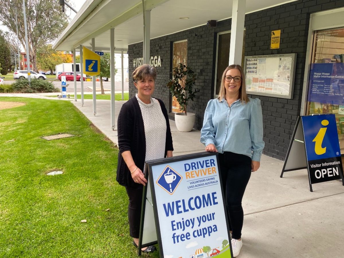 Two women stand beside a Driver Reviver sign