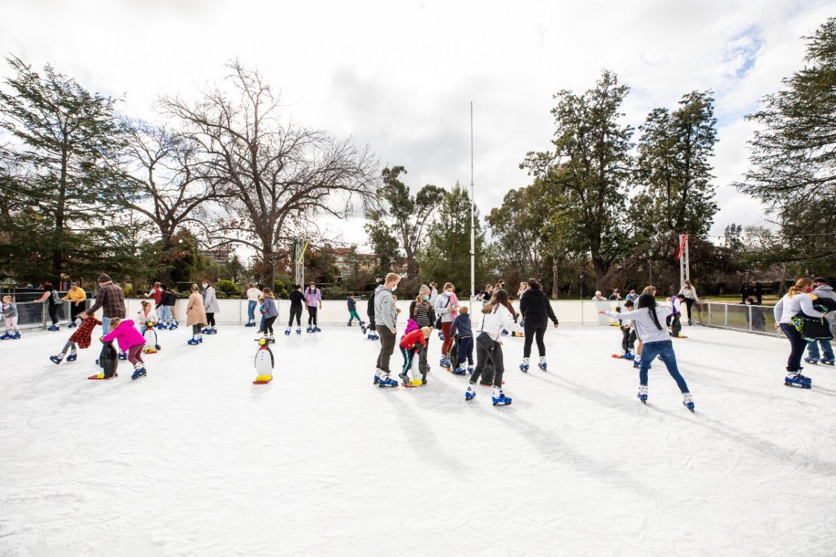 People ice skating on an outdoor ice rink during a cloudy day