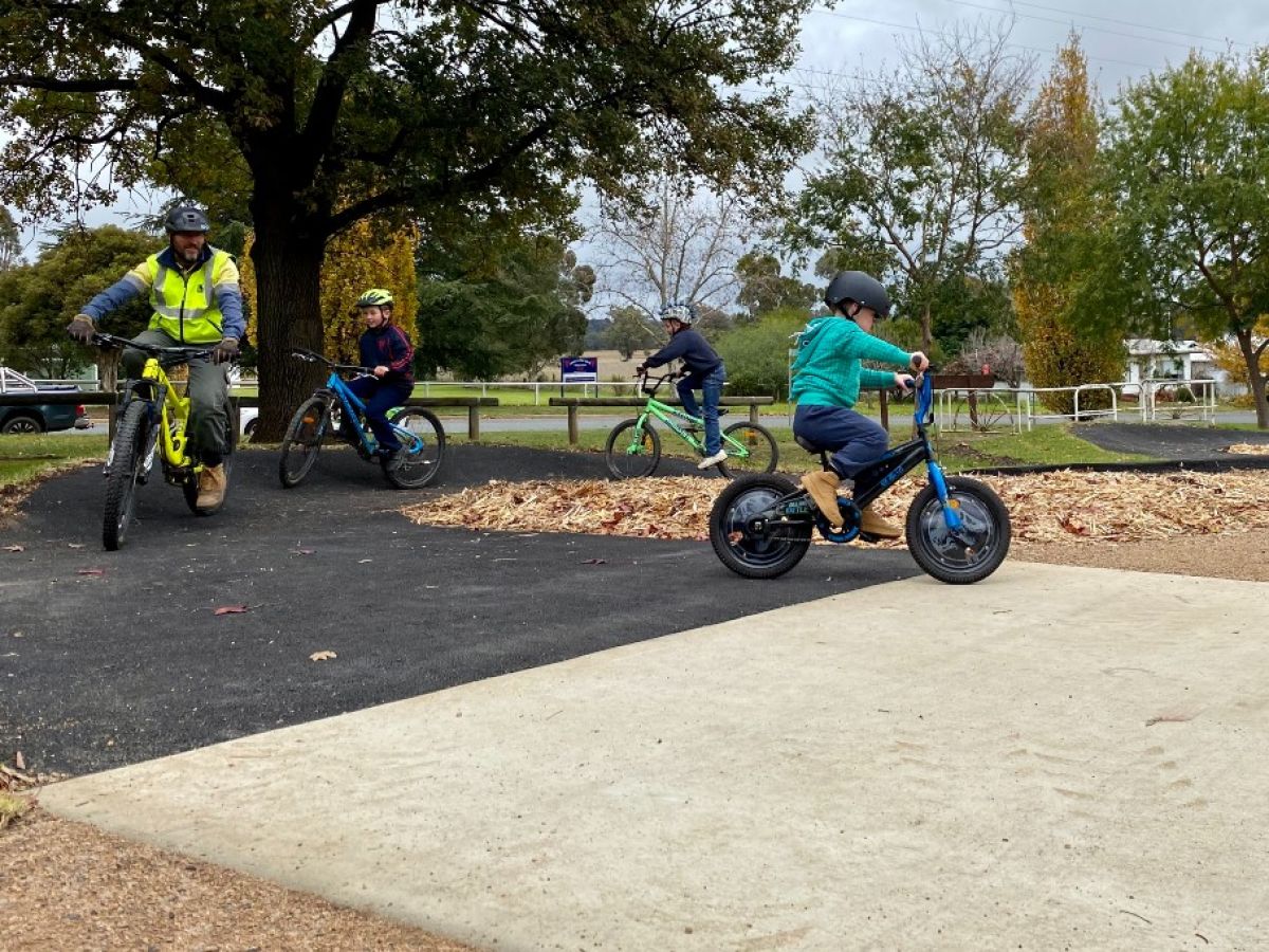 A small child rides a bike on a track in front of older riders