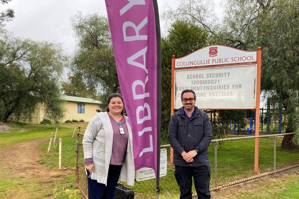 Man and woman standing beside Collingullie Primary School sign with Library banner