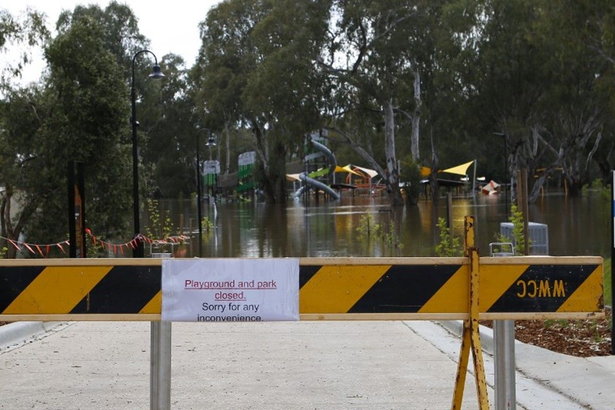 Closed sign on barriers with Riverside playground in flood waters in background