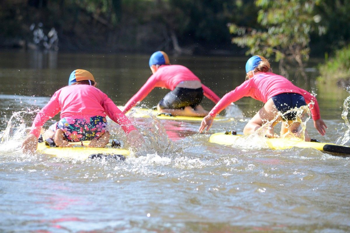 Rear view of three children on rescue boards paddling in river