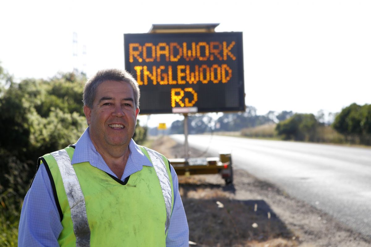 Warren Faulkner in hi-vis vest standing in front of VMS board beside road