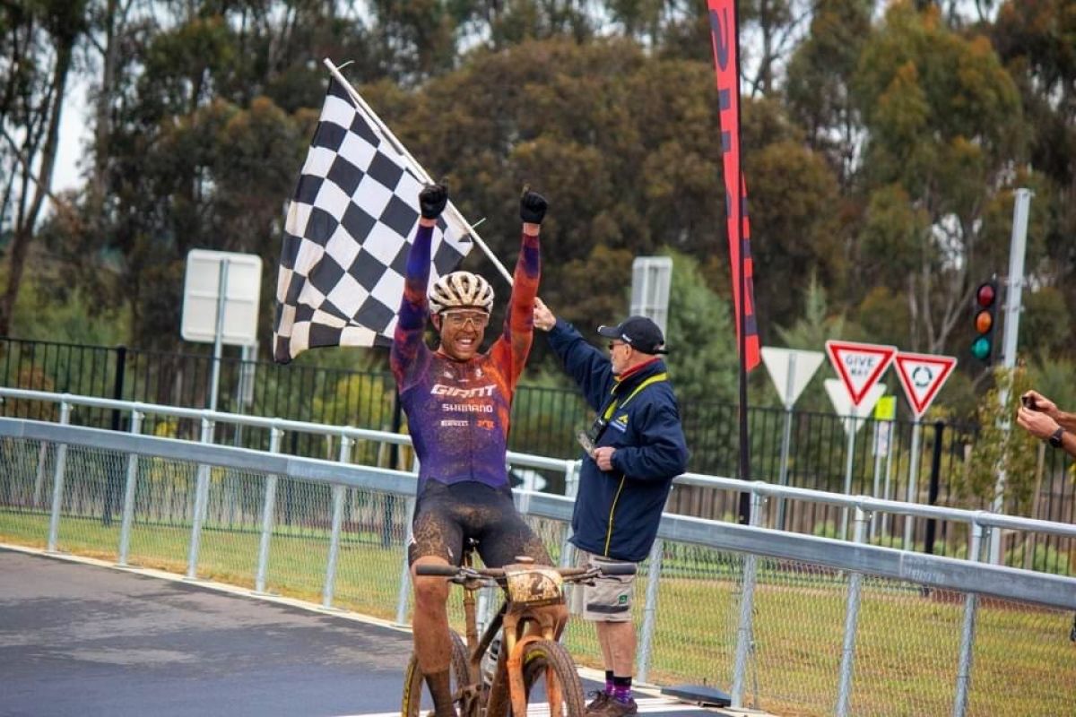 Winning cyclist on velodrome, holding checkered / chequered flag