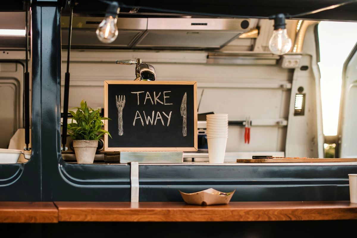 Blackboard sign with 'take away' written on it in white chalk on stand in window of street food truck.